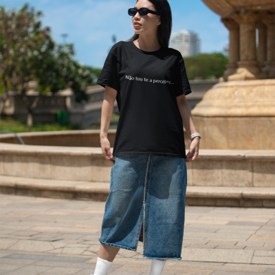 Mulher com t-shirt preta, saia jeans e sapatilhas brancas em espaço exterior com fonte de pedra