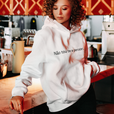 Casaco branco com capuz e texto 'Não tou te a perceber...' usado por mulher em cozinha/bar
