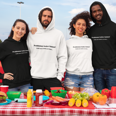 Quatro jovens com sweats pretas e brancas com texto, posando junto a mesa com toalha xadrez e comida.