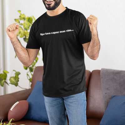 Homem com camisola preta e texto branco 'Não tava capaz mas vim...' em sala com sofá e snacks