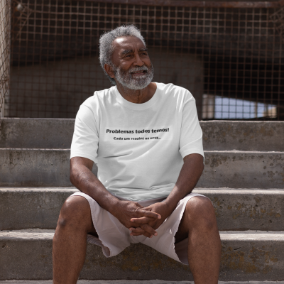 Homem sentado em escadas de cimento com t-shirt branca com texto em português