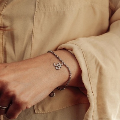 Pulseira prateada com pendente símbolo Om usada no pulso com camisola bege