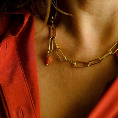 Colar dourado com elos grandes e pendente em pedra sobre pele feminina e camisa laranja