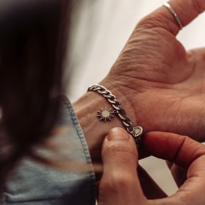 Pulseira prateada com pendente em forma de sol no pulso de uma pessoa