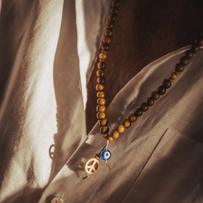 Colar de contas castanhas com pendentes em símbolo da paz e olho azul sobre camisa branca