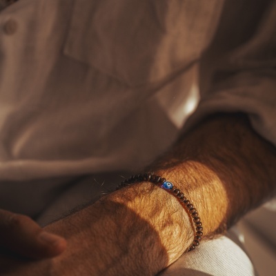 Pulseira masculina com contas castanhas e conta azul com olho no pulso