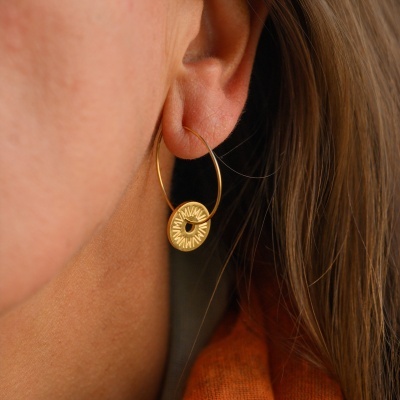 Brinco de argola dourada com pendente circular decorativo na orelha