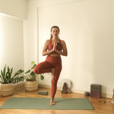 Mulher a fazer yoga em tapete verde numa sala com plantas e decorações
