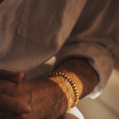 Pulseira dourada com contas e detalhe branco usada no pulso de homem com camisa bege