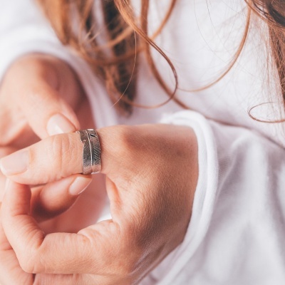 Anel de metal prateado com design de pena num dedo da mão