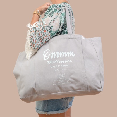 Mala grande de tecido cinzento claro com estampagem branca e pessoa a segurá-la