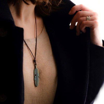 Colar com pendente em forma de pena verde e castanha sobre camisola bege e casaco preto