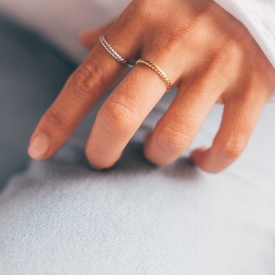 Mão com dois anéis, um dourado e outro prateado, sobre tecido azul claro