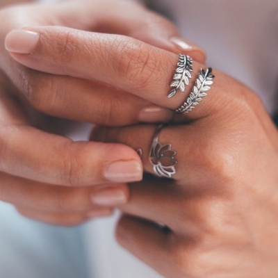 Anéis prateados com design de folhas e flor em dedos de mão com unhas nude
