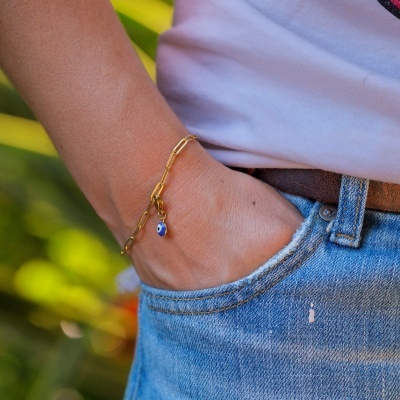 Pulseira dourada com pendente de olho azul no pulso