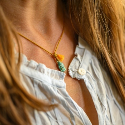 Colar artesanal com pendente verde e penduricalho amarelo no pescoço de mulher com camisa branca