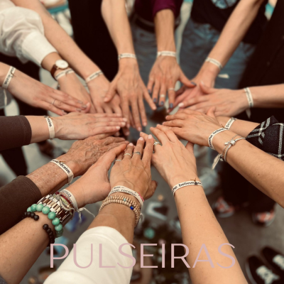 Mãos femininas em círculo usando pulseiras brancas com texto e palavra PULSEIRAS no rodapé