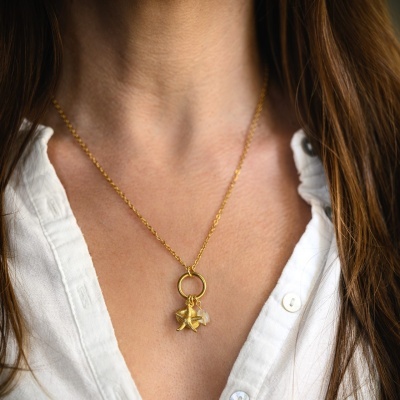 Colar dourado com pendentes de estrela e cristal numa mulher de camisa branca
