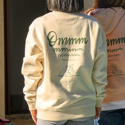Foto de costas de sweatshirt creme com texto 'Ommmm' e desenho de gato sobre tapete de ioga