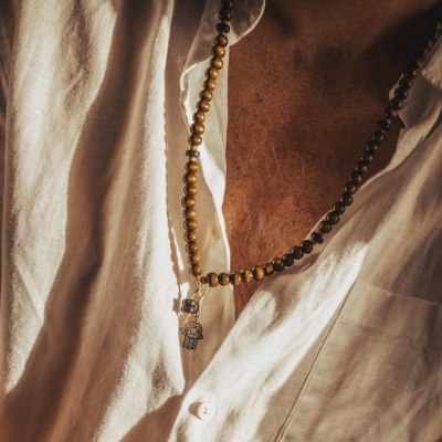 Colar de contas com pendente em forma de mão usado sobre camisa branca