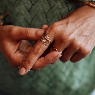 Anel dourado em formato de folhas num dedo, mãos femininas com fundo verde