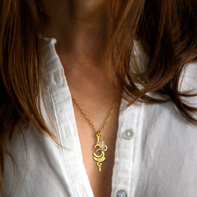 Colar dourado com pendente geométrico usado por mulher com camisa branca