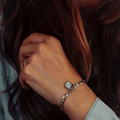 Pulseira prateada com pingente em forma de olho num pulso feminino.