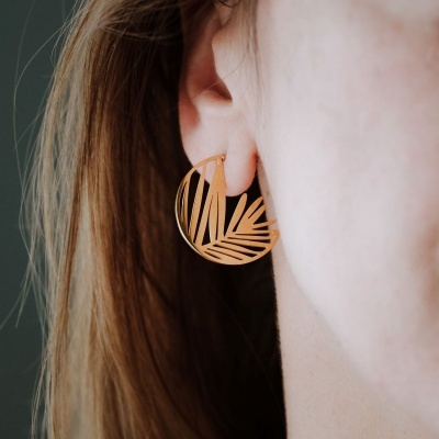 Brinco dourado com design de folhas em círculo na orelha de mulher
