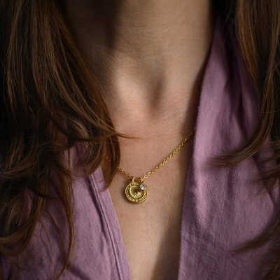 Colar dourado com pingente circular numa mulher com camiseta roxa