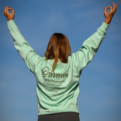 Pessoa de costas a vestir sweatshirt verde água com ilustração e texto na parte traseira sob céu azul
