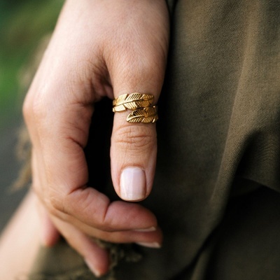 Anel dourado com design de penas no dedo polegar