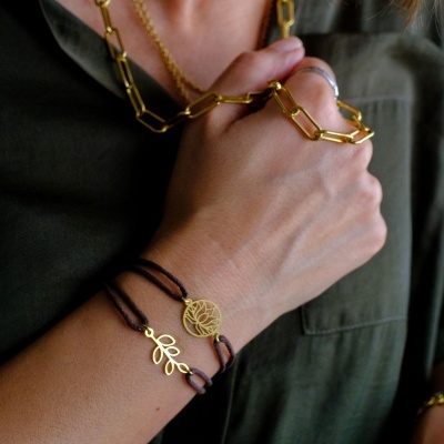 Pulseiras e colar dourados com detalhes de folha e padrão floral em fundo de camisa verde escura