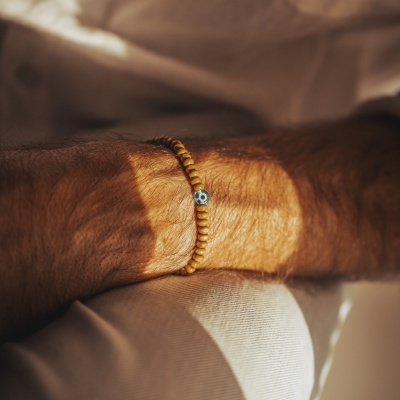 Pulseira de contas de madeira clara com conta azul e branca no pulso de um homem