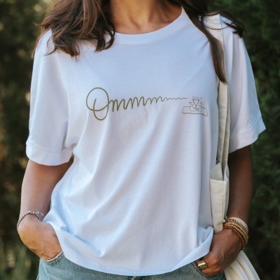T-shirt branca com estampa dourada de 'Ommmmmm' e ilustração minimalista