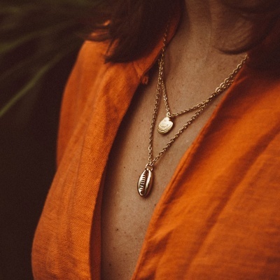 Colar dourado com pendentes de conchas usado com camisa laranja