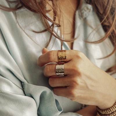 Anéis largos martelados dourado e prateado na mão de uma pessoa com vestido azul claro