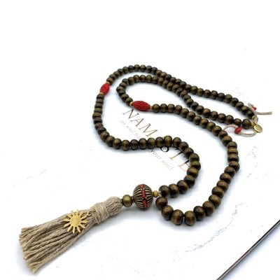 Colar de contas marrons e vermelhas com franjas bege e pingente em forma de sol sobre fundo branco
