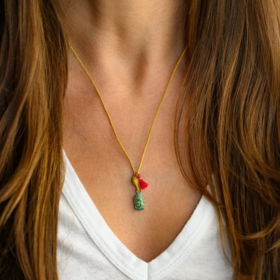 Colar amarelo com pendente verde, detalhes dourados e vermelho em pescoço feminino