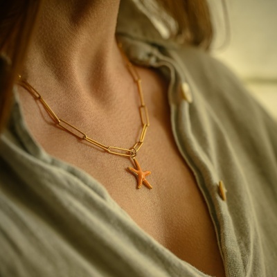 Colar dourado com pendente estrela do mar laranja num pescoço.