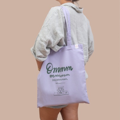 Saco de tecido lilás com estampa e alças longas usado no ombro por pessoa com camisa cinza claro