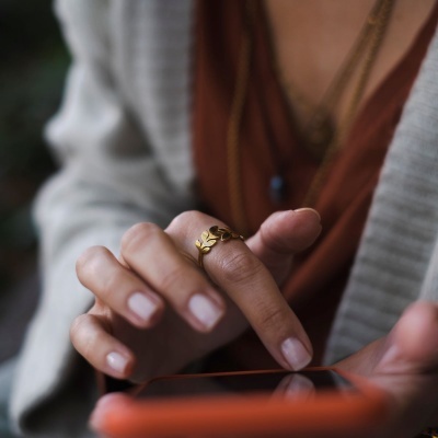 Mão com anel dourado segurando smartphone laranja em fundo desfocado
