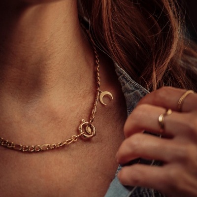 Colar dourado com pendente de lua no pescoço e anéis dourados
