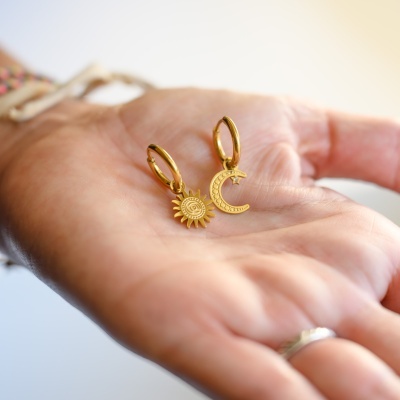 Brincos dourados de sol e lua na mão