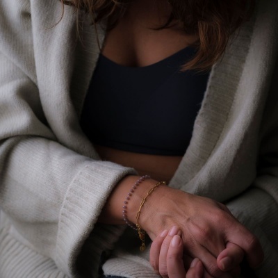 Pulseiras dourada e roxa num pulso com casaco cinzento claro e top preto