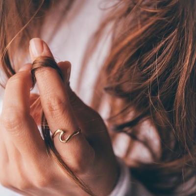 Mão com anel dourado segurando cabelo castanho claro
