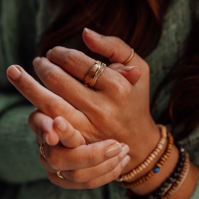 Mão feminina com anel pena dourado e pulseiras de contas
