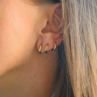 Três brincos pequenos dourados em argola no lóbulo da orelha