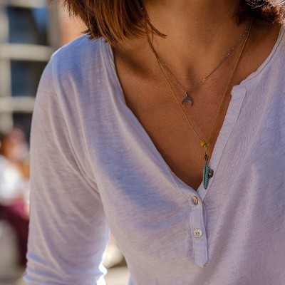 Mulher com blusa branca e dois colares delicados ao ar livre