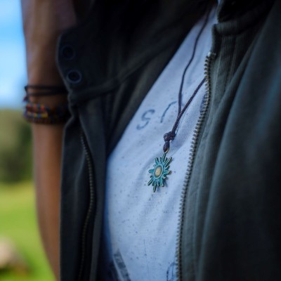 Colar com pendente de sol turquesa e dourado em cordão castanho junto a roupa casual verde e branca