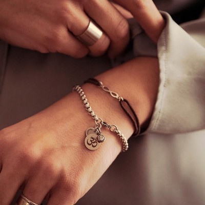 Pulseira de prata com pendente OM e pulseira castanha com infinito no pulso esquerdo